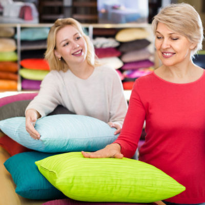 Adult girl and aged mother choosing pillows in home textile shop